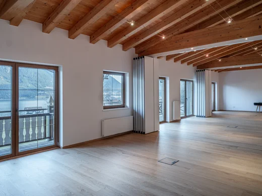 Großer leerer Raum mit Holzdecke und Blick auf Bergsee durch Fenster