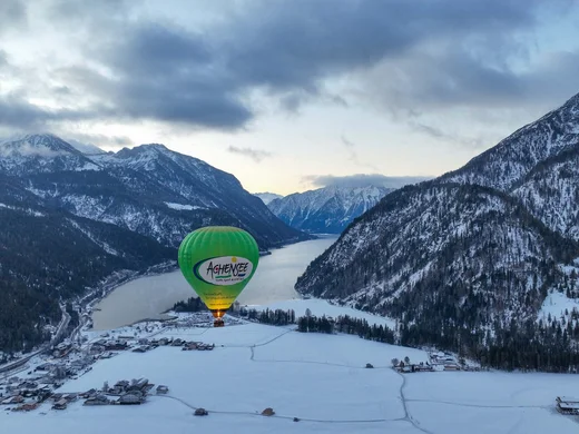 Den Achensee entdecken Heißluftballon über verschneitem Tal und Berglandschaft im Winter
