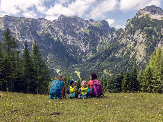 Euer Familienhotel am Achensee Familie mit Rucksäcken sitzt auf einer Wiese mit Blick auf Berge und Wald