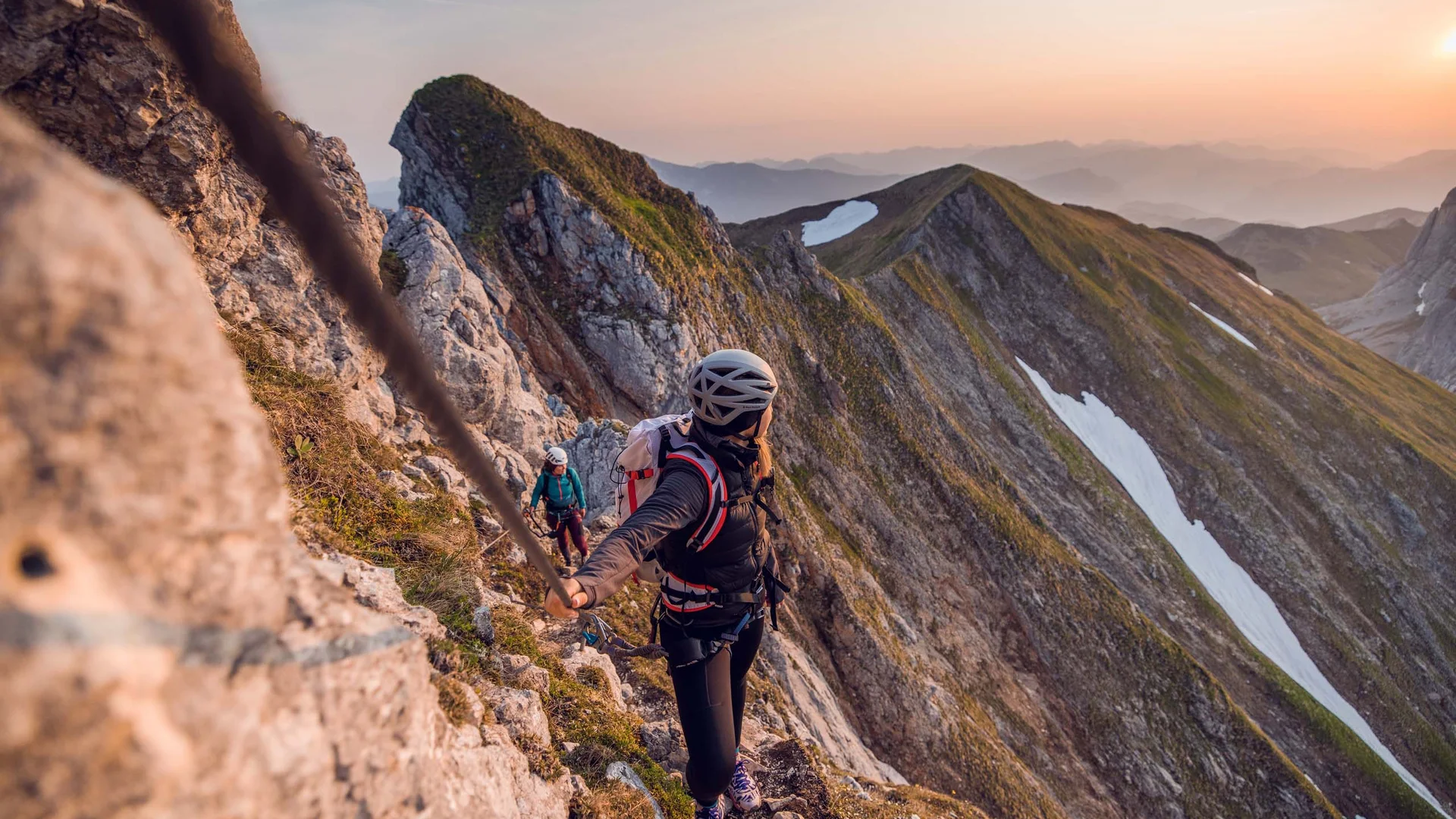Wanderhotel Tirol: durchs Karwendel wandern und biken Kletterer sichern sich an Seil an steiler Felswand bei Sonnenuntergang in den Bergen
