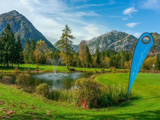Euer Golfhotel am Achensee Golfplatz mit Teich, Springbrunnen und Bergen im Hintergrund bei sonnigem Wetter