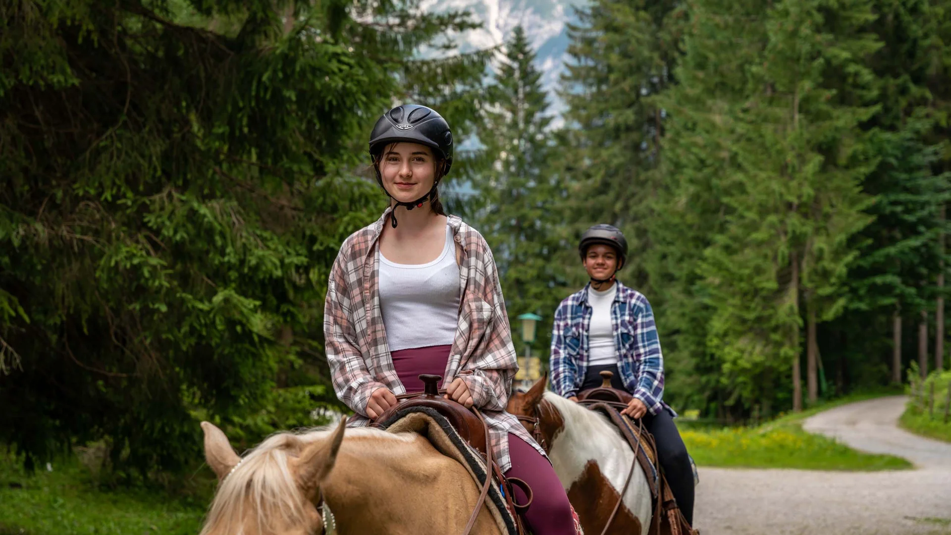Familienhotel mit Ponyreiten am Achensee | Wiesenhof Pertisau Zwei Reiter mit Helmen reiten Pferde auf einem Waldweg