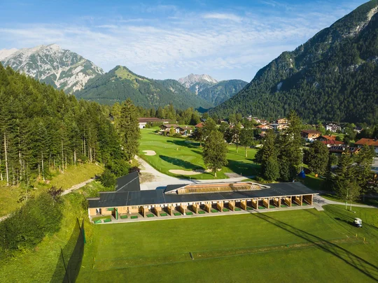 Euer Golfhotel am Achensee Golfplatz mit Driving Range im Bergtal und Dorf im Hintergrund