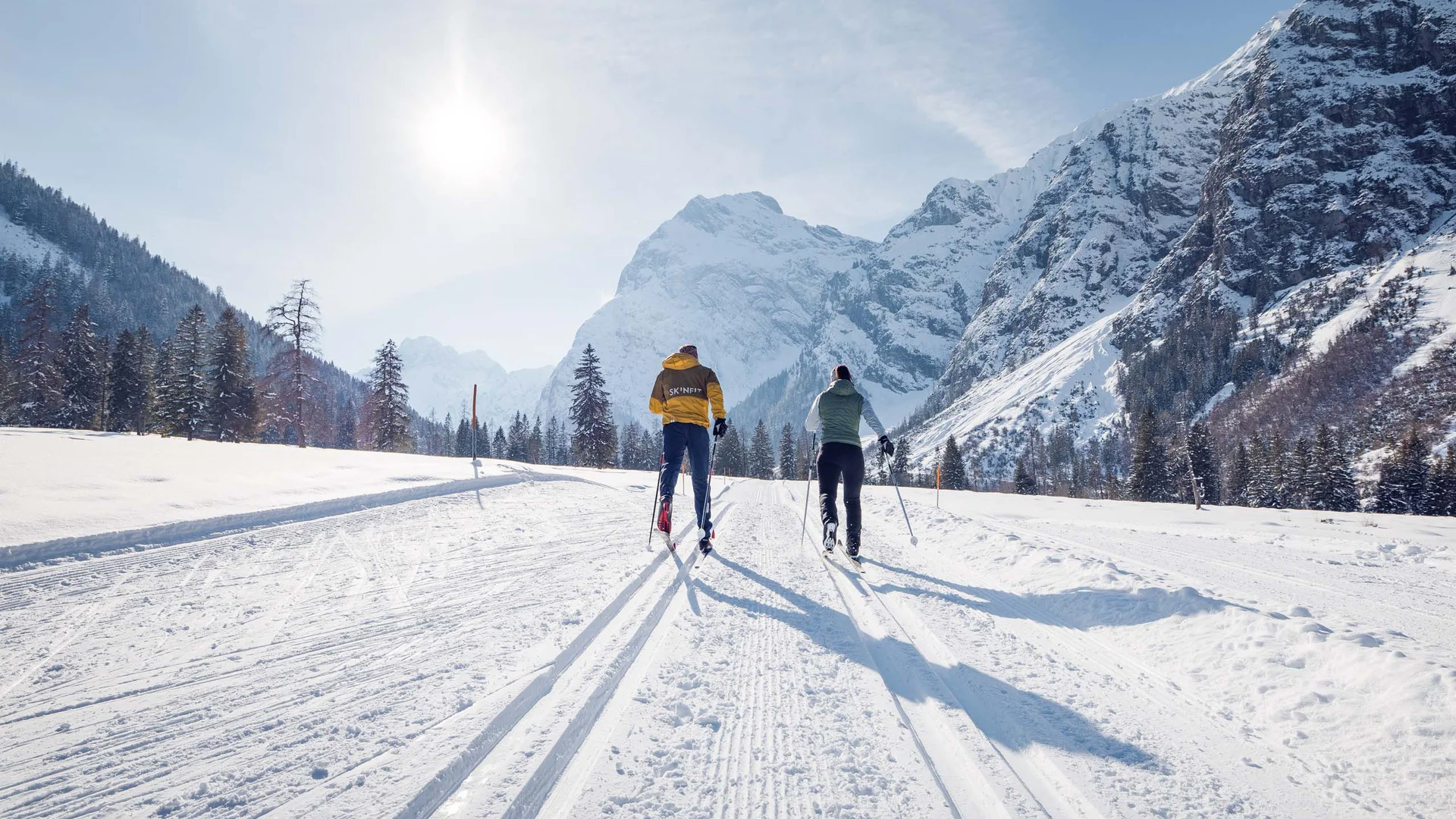 Den Achensee entdecken Zwei Skifahrer fahren auf verschneiter Berglandschaft bei sonnigem Wetter
