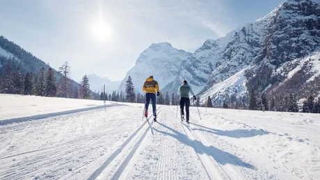 Zwei Skifahrer fahren auf verschneiter Berglandschaft bei sonnigem Wetter