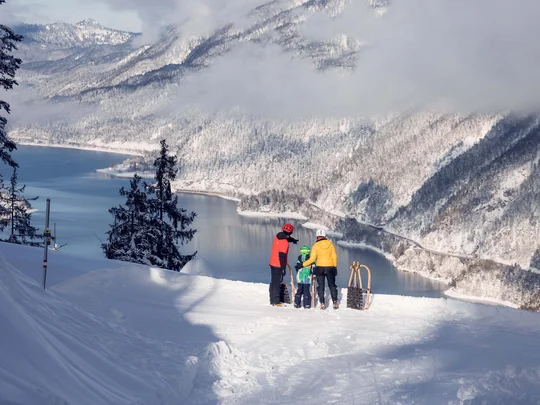 Wanderhotel Tirol: durchs Karwendel wandern und biken Drei Personen mit Schlitten blicken auf verschneite Berge und einen Fluss
