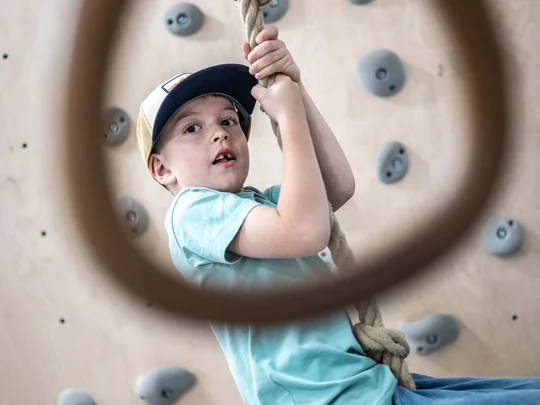 Euer Familienhotel am Achensee Junge klettert an Indoor-Kletterwand und hält ein Seil fest