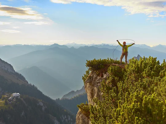 Wanderhotel Tirol: durchs Karwendel wandern und biken Bergsteiger steht auf Felsen mit Seil vor bewaldeten Bergen und blauem Himmel