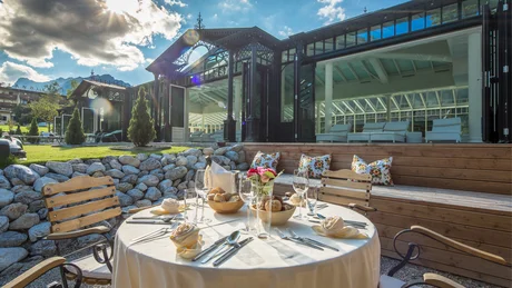 Gedeckter Außentisch mit Stühlen und Glasfassade im Hintergrund bei Sonnenschein