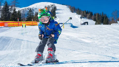 Kind fährt Ski auf schneebedeckter Piste mit Drachenhelm und blauem Mantel