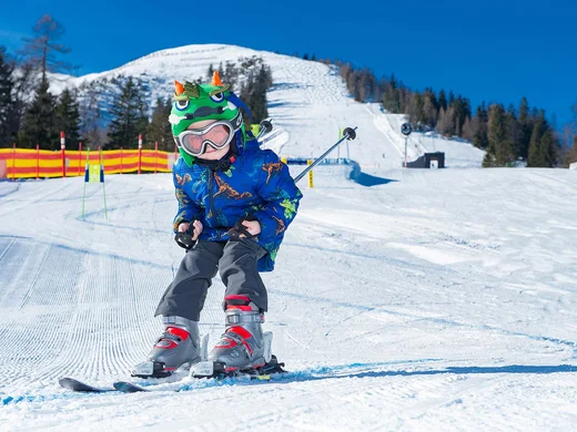 Euer Familienhotel am Achensee Kind fährt Ski auf schneebedeckter Piste mit Drachenhelm und blauem Mantel