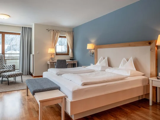 Zimmer und Suiten im Wiesenhof Gemütliches Hotelzimmer mit Doppelbett, Sesseln und Fenster mit Blick auf verschneite Berge