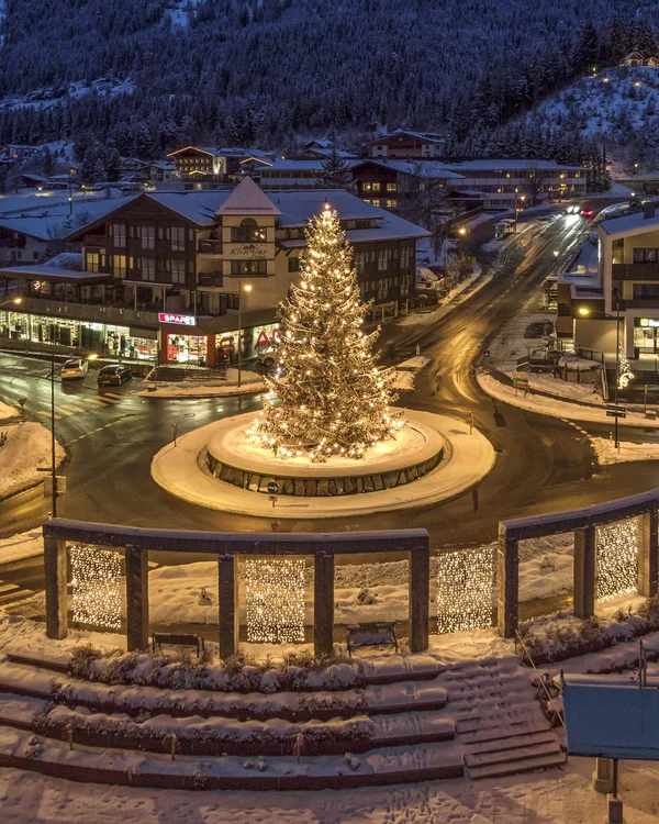 Weihnachtsbaum beleuchtet auf einem Kreisverkehr in einem verschneiten Dorf bei Nacht