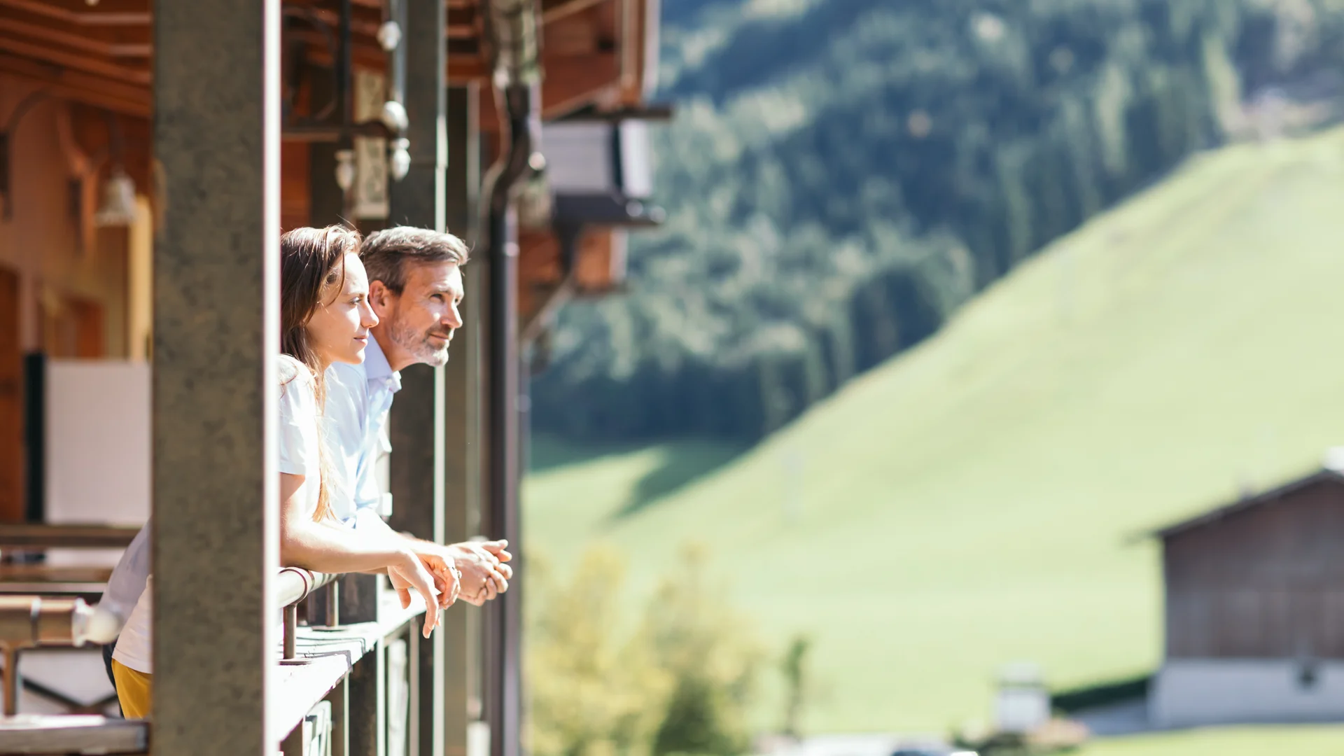 Das 4-Sterne-Hotel am Achensee: der Wiesenhof Paar lehnt auf Balkon mit Bergblick an sonnigem Tag