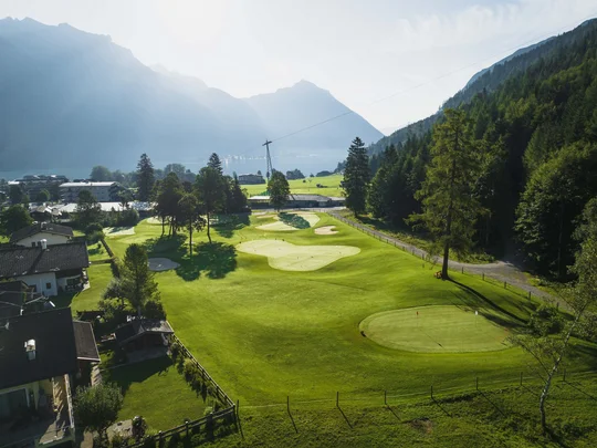 Euer Golfhotel am Achensee Golfplatz in einem Bergtal mit Bäumen und Häusern bei klarem Wetter