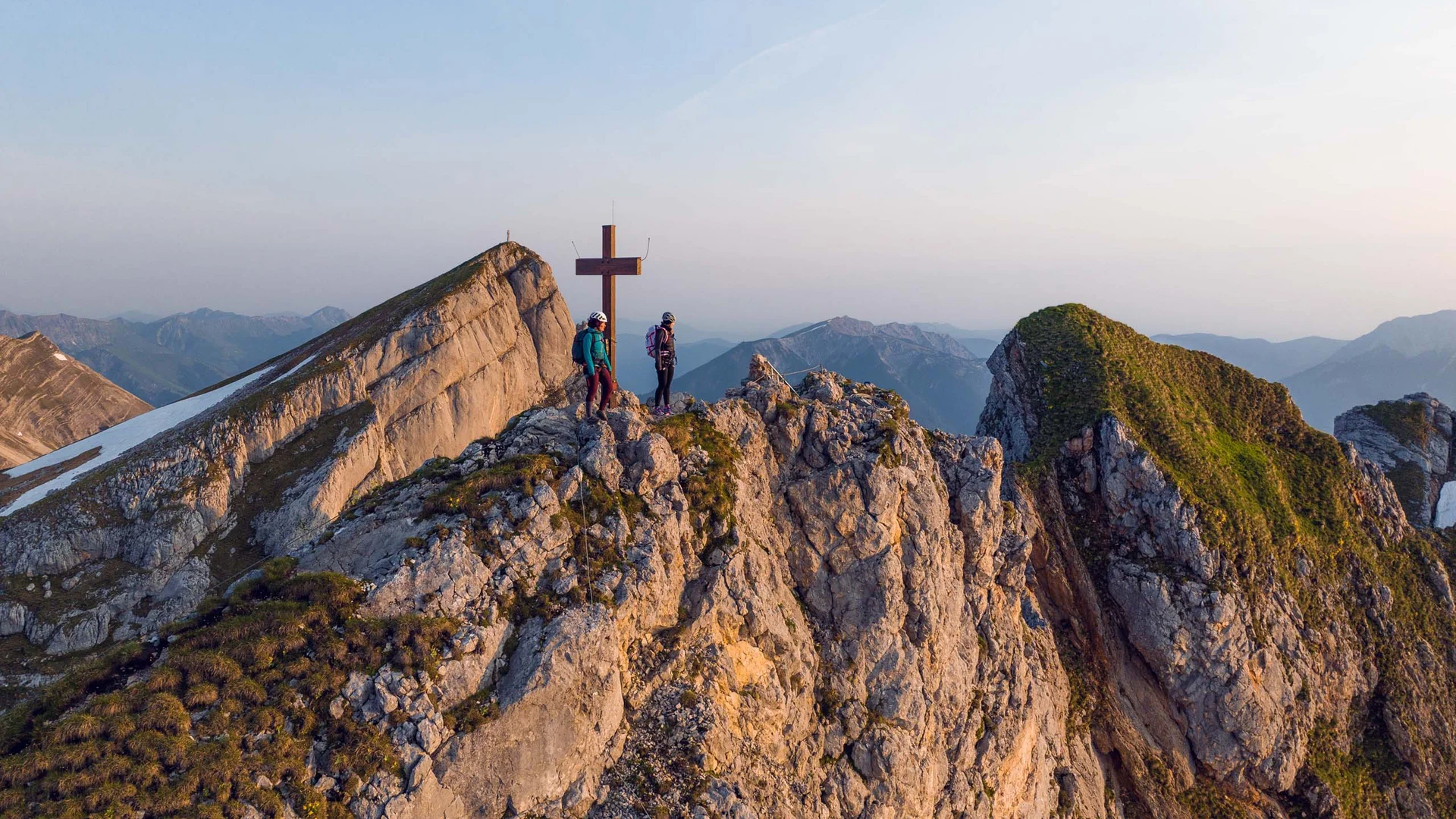 Den Achensee entdecken Zwei Bergsteiger stehen am Gipfelkreuz auf felsigem Berggipfel bei klarem Himmel