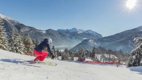 Skifahrer in roter Hose fährt an sonnigem Tag den schneebedeckten Berg hinunter mit Bergen im Hintergrund