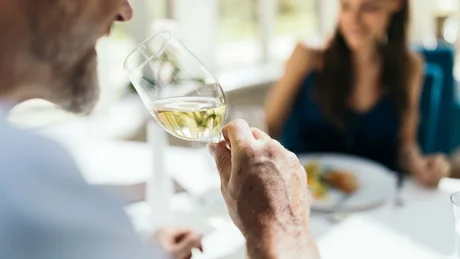 Mann hält Weinglas mit weißem Wein bei einem Essensgespräch