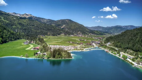 Bergsee mit grünem Tal, Wäldern und kleinen Dörfern bei klarem Himmel
