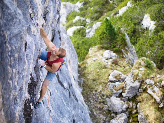 Wanderhotel Tirol: durchs Karwendel wandern und biken Mann klettert an steiler Felswand in bewaldeter Bergregion