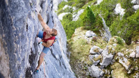 Mann klettert an steiler Felswand in bewaldeter Bergregion