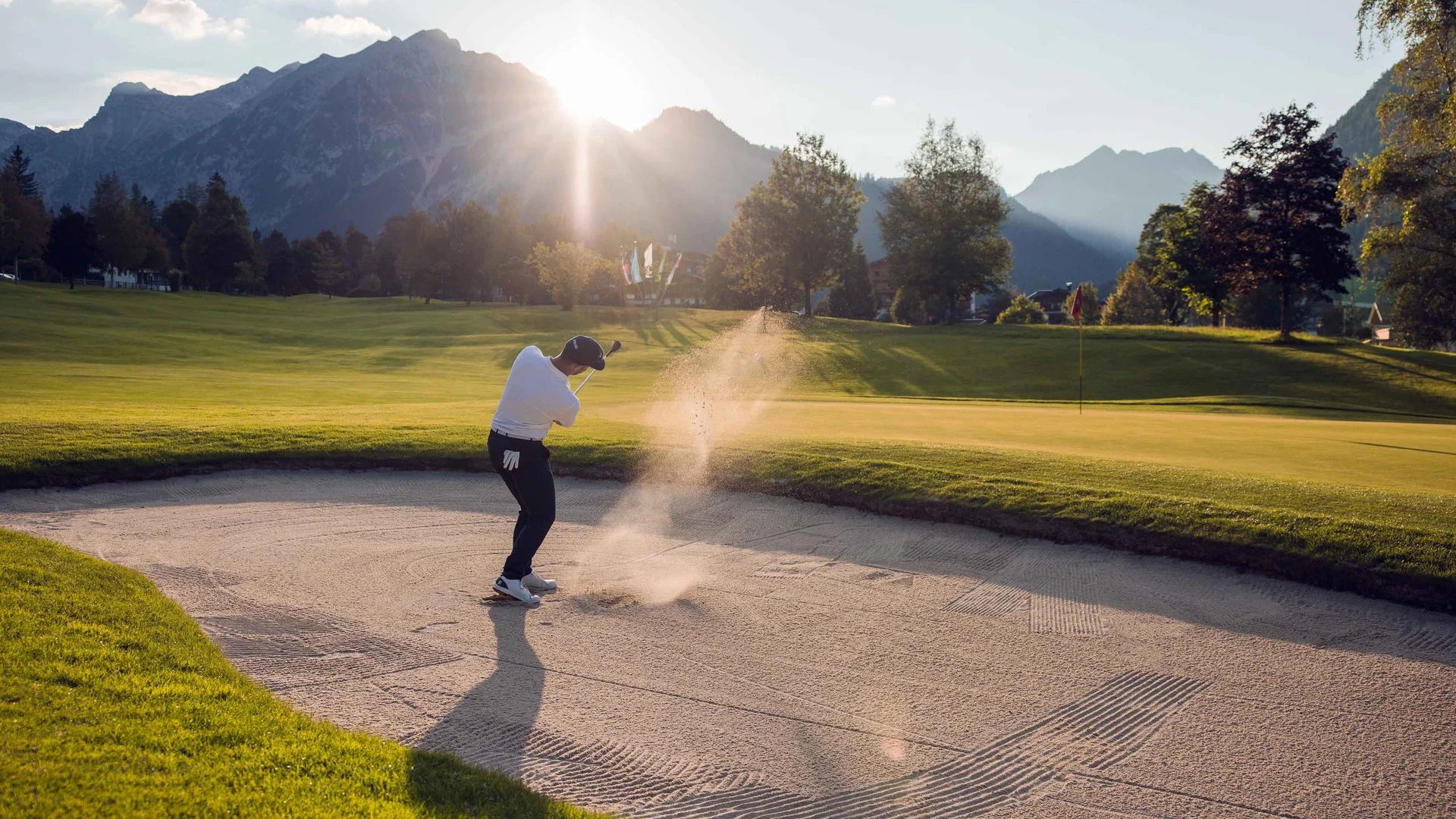 Den Achensee entdecken Golfer schlägt Ball aus Sandbunker mit Bergen und Sonne im Hintergrund