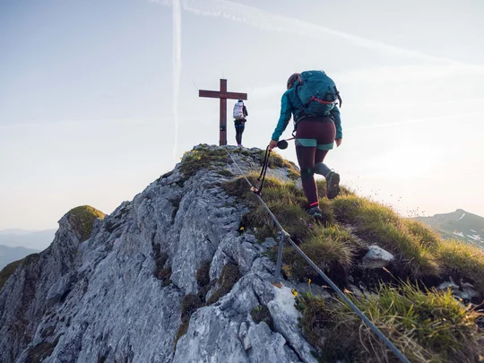 Wanderhotel Tirol: durchs Karwendel wandern und biken Zwei Wanderer steigen zum Gipfelkreuz auf einem felsigen Berggipfel