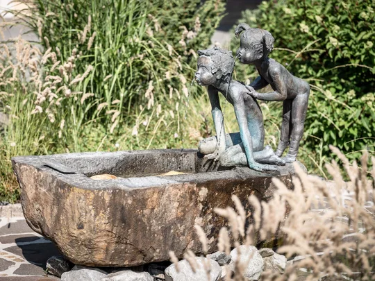 Der Wiesenhof in Pertisau und die Familie Entner mit Team Skulptur von zwei Kindern an einem steinernen Becken mit Wasser im Garten