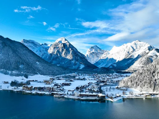 In, auf und rund um den Achensee Winterliches Dorf am See vor verschneiten Bergen unter blauem Himmel