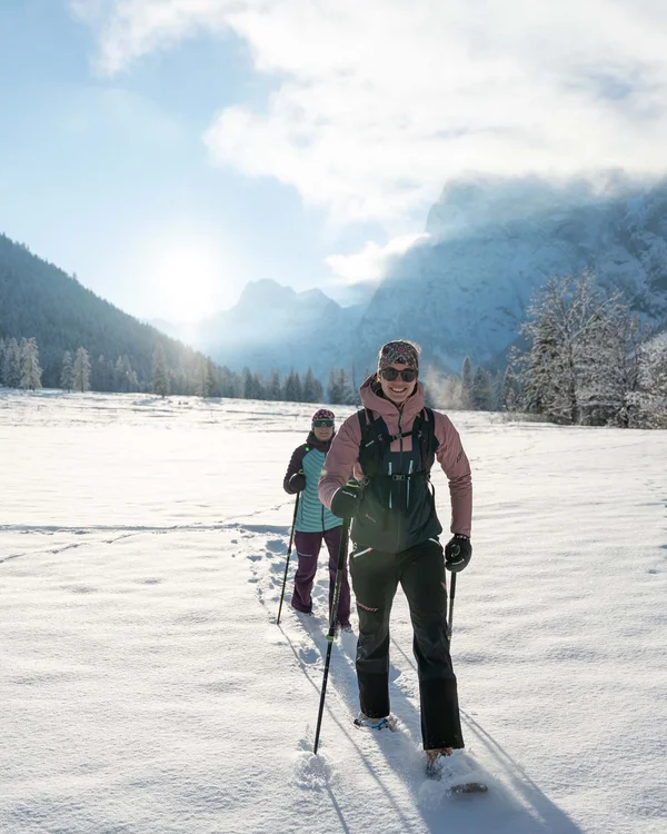Zwei Frauen wandern mit Schneeschuhen im sonnigen schneebedeckten Tal