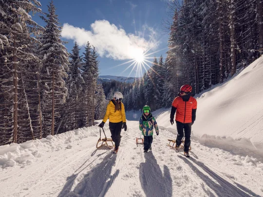 Wanderhotel Tirol: durchs Karwendel wandern und biken Familie mit Schlitten wandert bei Sonnenschein durch verschneiten Wald
