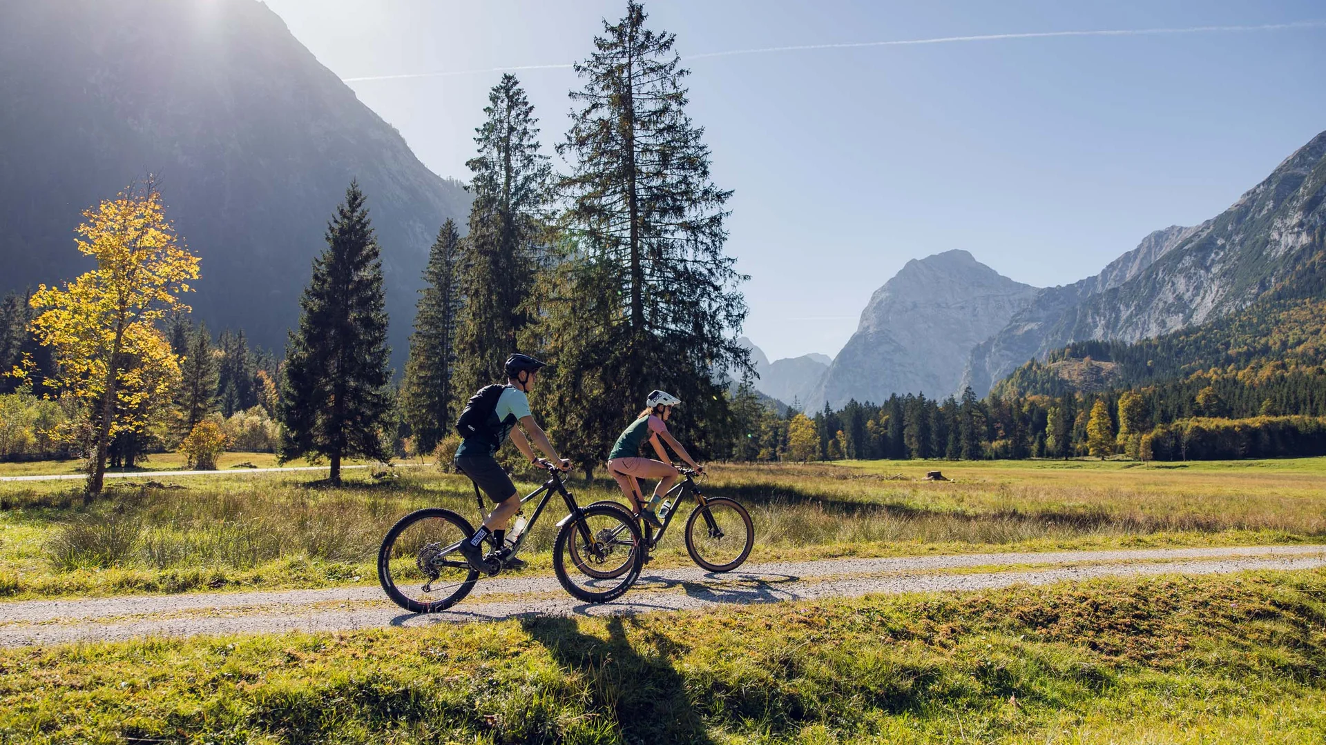 Zwei Radfahrer fahren auf einem Weg in bergiger Herbstlandschaft