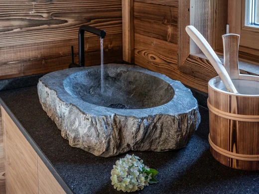 Seminarräume Achensee | Tagungshotel Wiesenhof Tirol Steinwaschbecken mit Wasserhahn und Holzgefäß auf schwarzer Arbeitsplatte