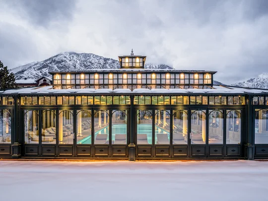 Beleuchtetes Gewächshaus mit Innenpool im verschneiten Berggebiet bei Dämmerung