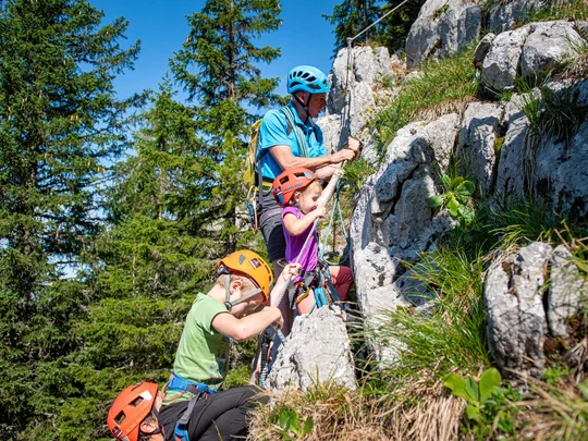 Euer Familienhotel am Achensee Erwachsener mit zwei Kindern klettert gesichert an einem Felsen im Wald