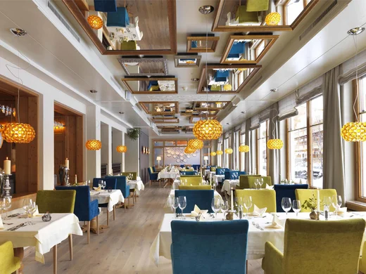 Das 4-Sterne-Hotel am Achensee: der Wiesenhof Helles Restaurant mit grünen und blauen Stühlen und Pendelleuchten