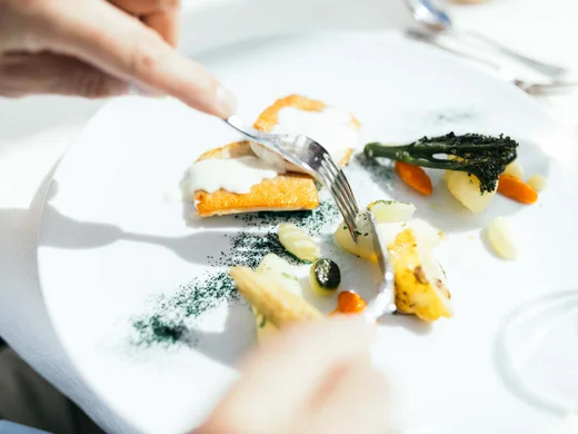 Person schneidet feines Gourmetgericht mit Gemüse und Sauce auf weißem Teller