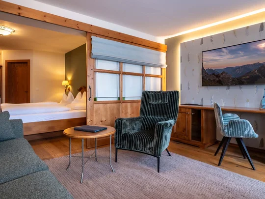 Zimmer und Suiten im Wiesenhof Gemütliches Hotelzimmer mit Sessel, Sofa, Holzschreibtisch und Schlafzimmerbereich