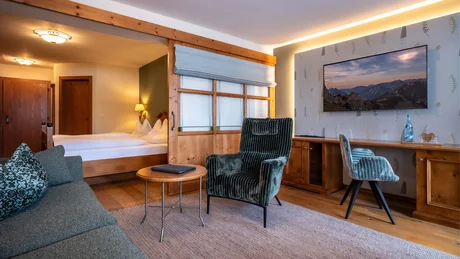 Gemütliches Hotelzimmer mit Sessel, Sofa, Holzschreibtisch und Schlafzimmerbereich