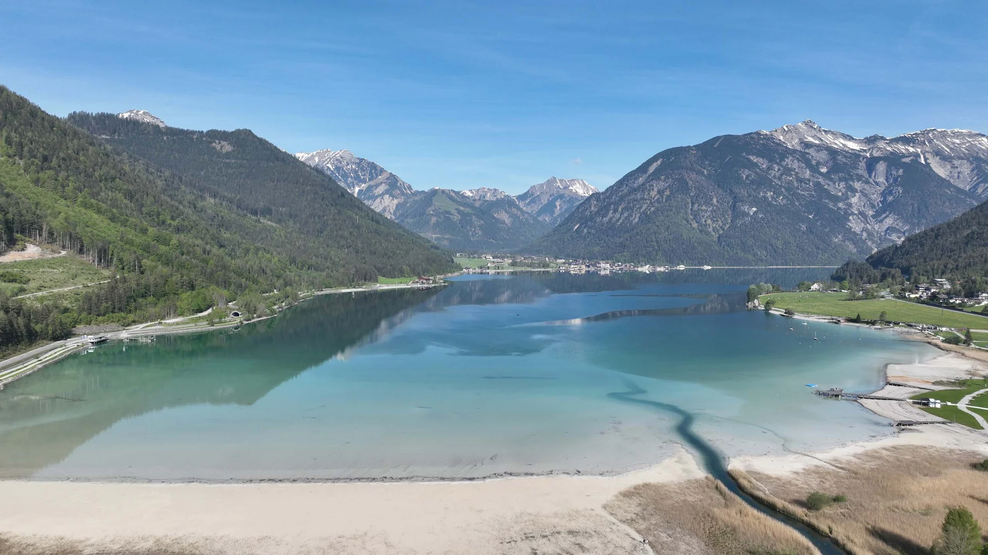 In, auf und rund um den Achensee Klarer Bergsee mit Sandstrand umgeben von bewaldeten Bergen unter blauem Himmel