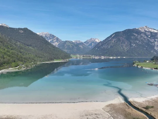 In, auf und rund um den Achensee Klarer Bergsee mit Sandstrand umgeben von bewaldeten Bergen unter blauem Himmel
