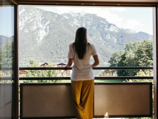 Zimmer und Suiten im Wiesenhof Frau sieht von Balkon auf Berge und Dorf in sonniger Landschaft