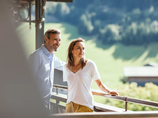 Das 4-Sterne-Hotel am Achensee: der Wiesenhof Paar steht auf Balkon mit Blick auf grüne Landschaft