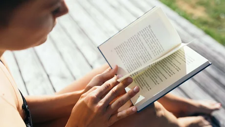Frau liest Buch im Freien auf Holzboden sitzend