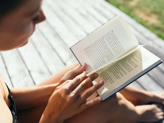 Eure Fragen – unsere Wiesenhof Antworten Frau liest Buch im Freien auf Holzboden sitzend