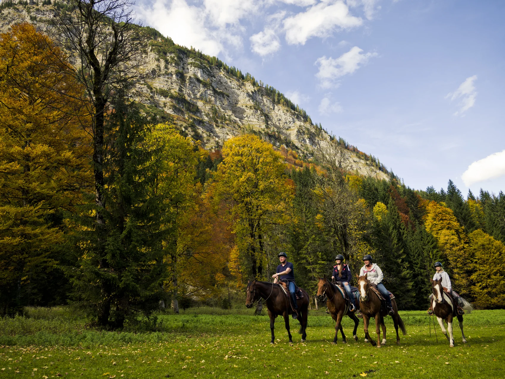 Familienhotel mit Ponyreiten am Achensee | Wiesenhof Pertisau Vier Personen reiten auf Pferden vor herbstlichen Bäumen und Bergkulisse