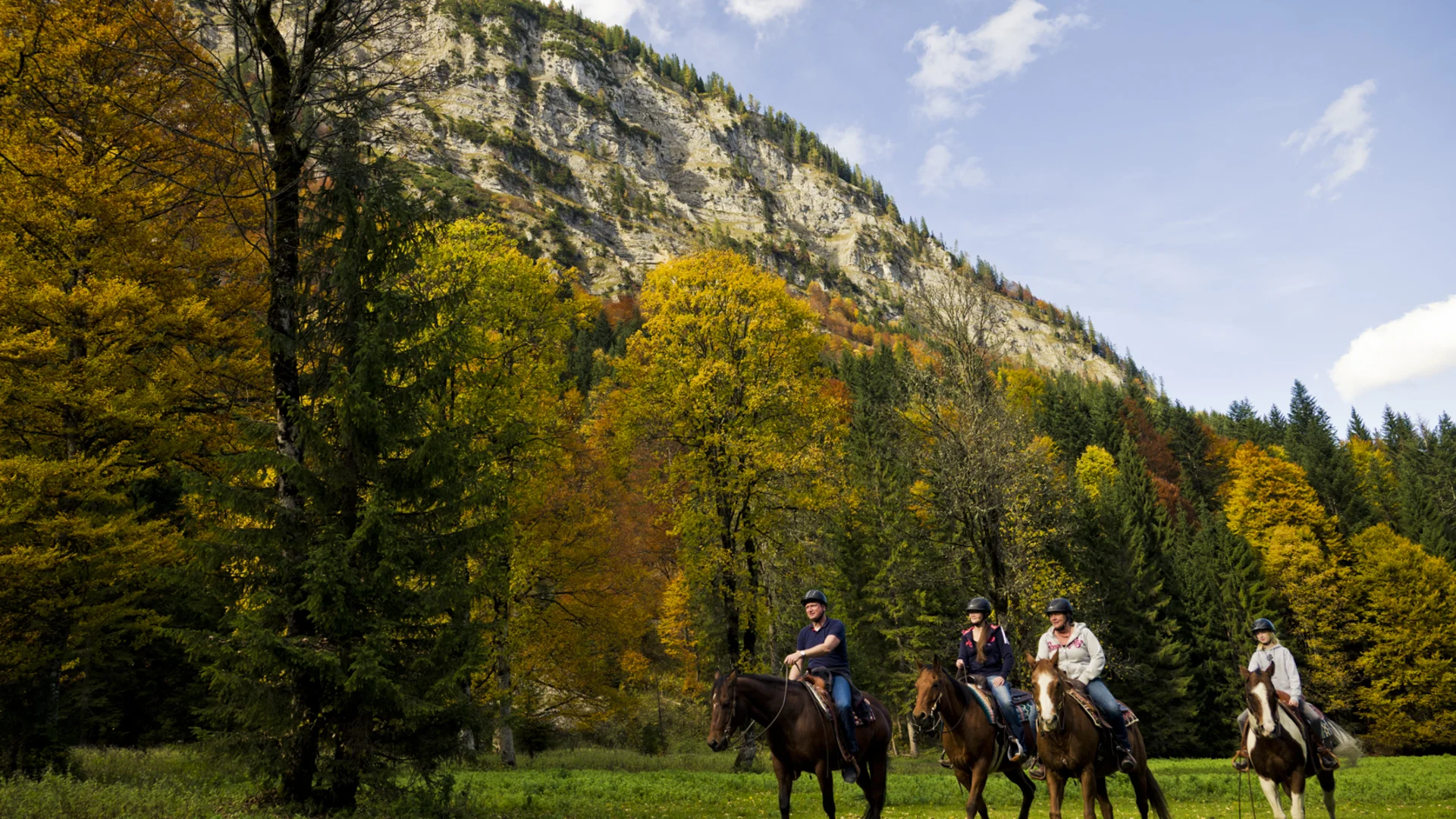 Familienhotel mit Ponyreiten am Achensee | Wiesenhof Pertisau Vier Personen reiten auf Pferden vor herbstlichen Bäumen und Bergkulisse