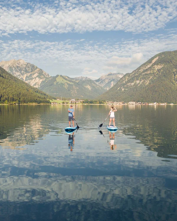 Zwei Personen auf Stand-up-Paddle-Boards auf einem stillen Bergsee bei bewölktem Himmel