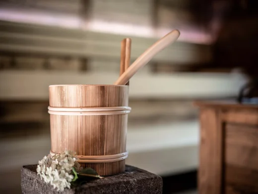Auf in ein romantisches Hotel in Tirol Traditioneller Holzsaunabecher mit Schöpfkelle und Blume auf Stein