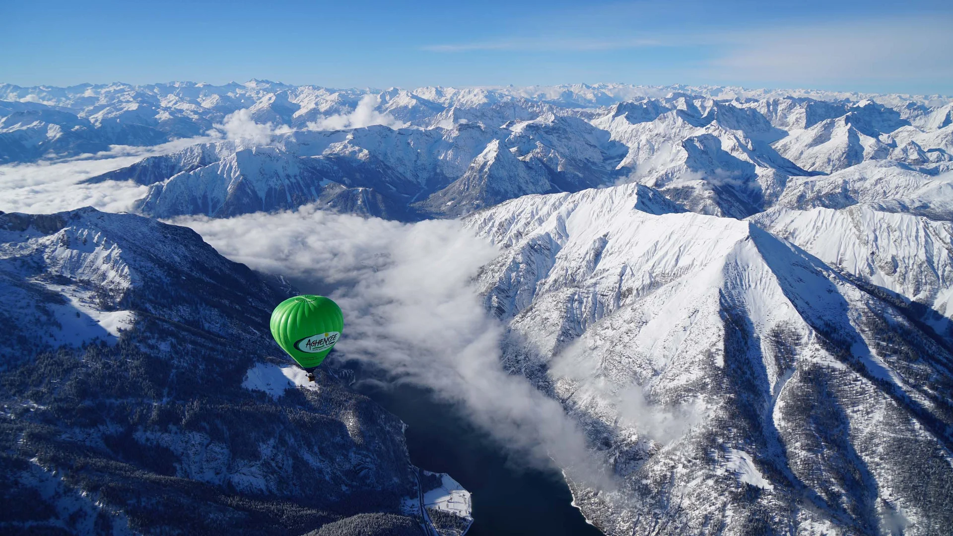 Den Achensee entdecken Grüner Heißluftballon über schneebedeckten Bergen und einem Flusstal